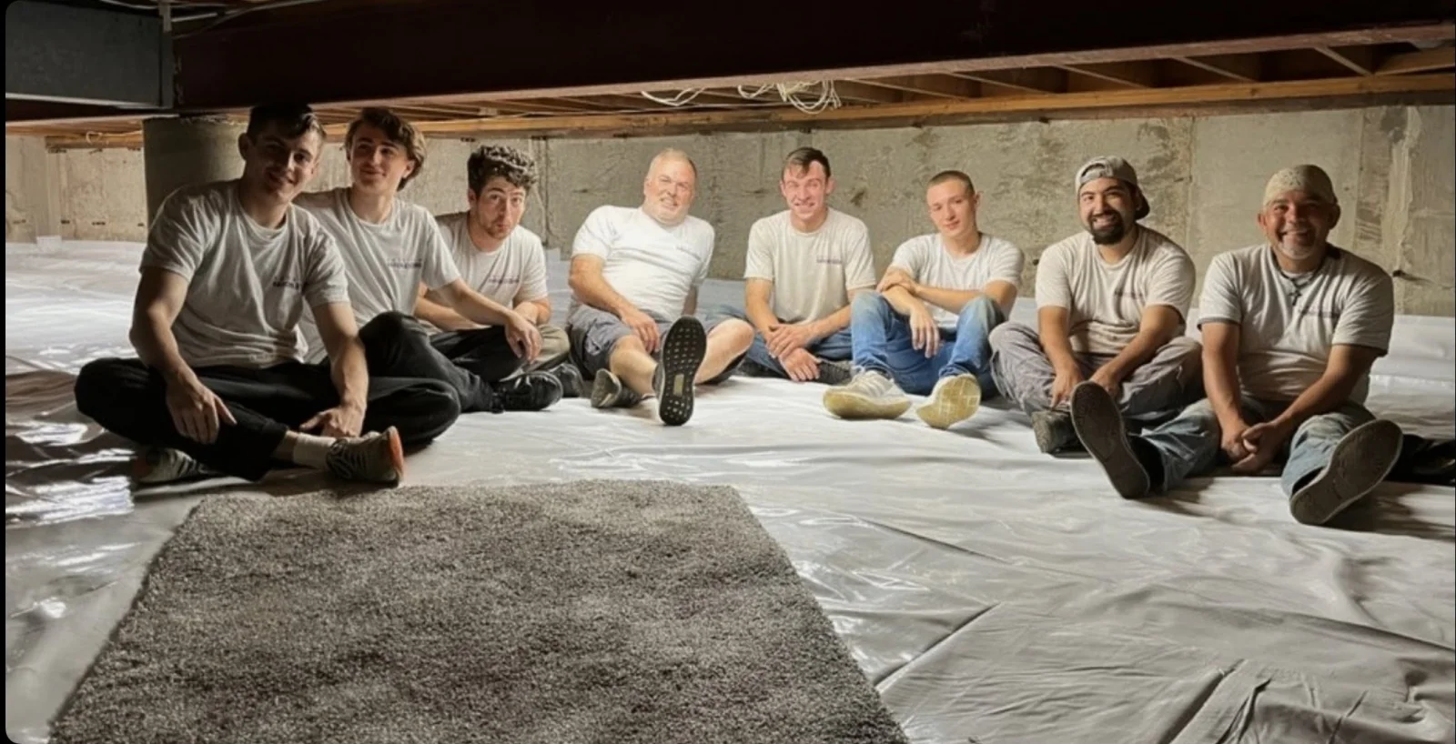 Eight members of the American Radon Systems crew sitting together in a fully encapsulated crawl space during a job in Palos Hills, Illinois.